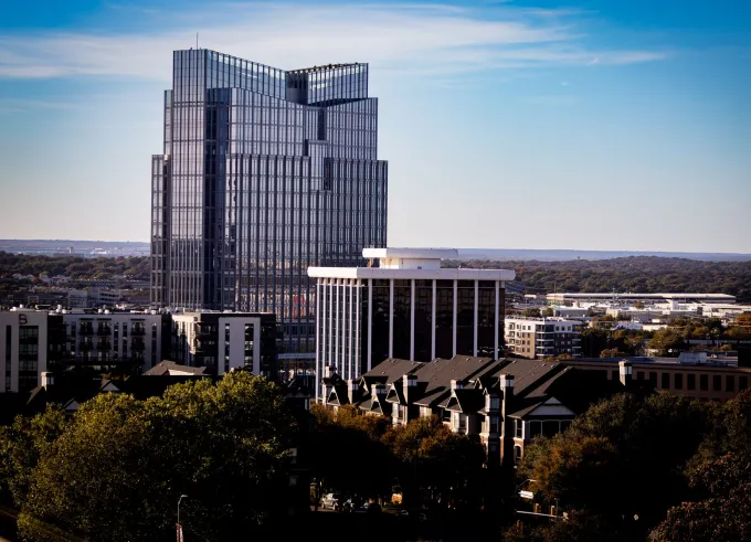 Glass office tower above the rooftops and trees of Fort Worth